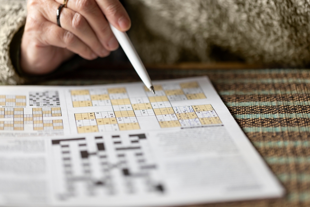 Sudoku brain game with numbers on a newspaper with a woman holding a pen in a cosy warm home. Great exercise for elderly people to keep a healthy active mind, reduce alzheimer and dementia
