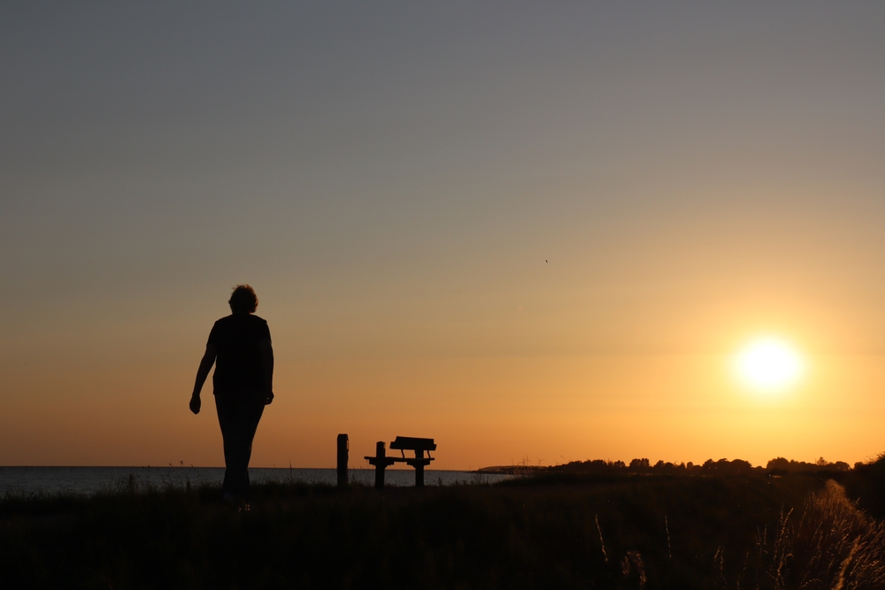 Black silhouette walking on ridge toward the sunset. Orange and blue sky.