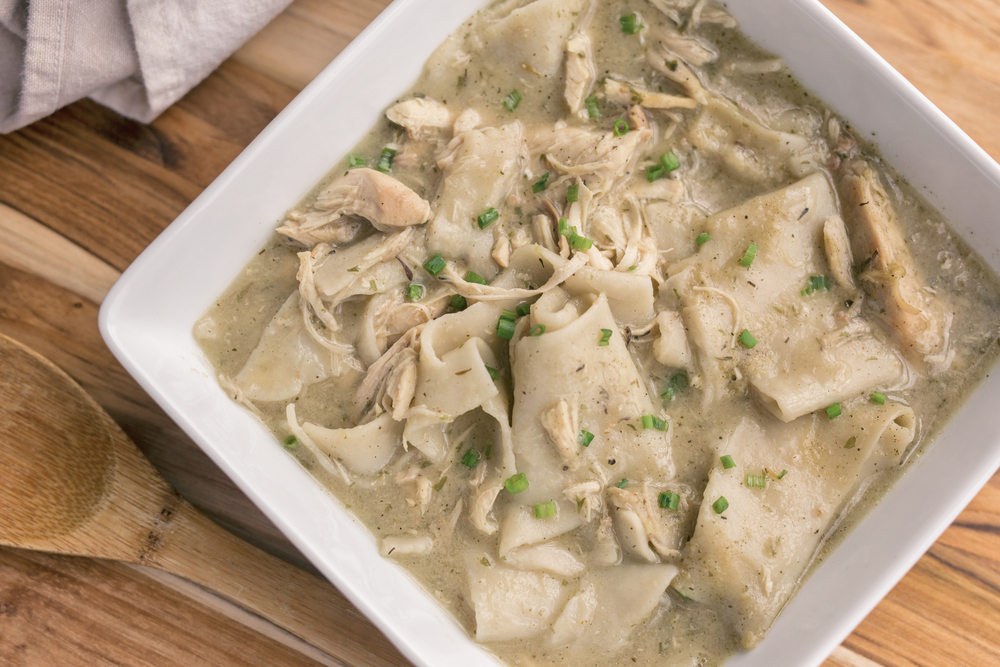 Southern style chicken and dumplings in a square bowl on a wood table. 