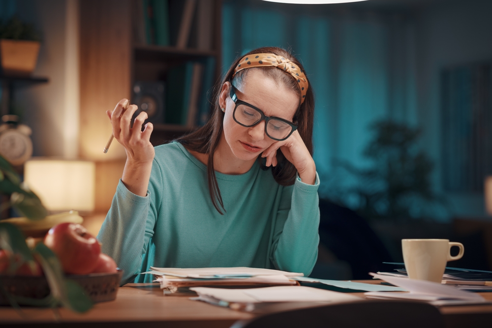 Bored woman checking bills and invoices at home, she is sitting at desk and reading paperwork