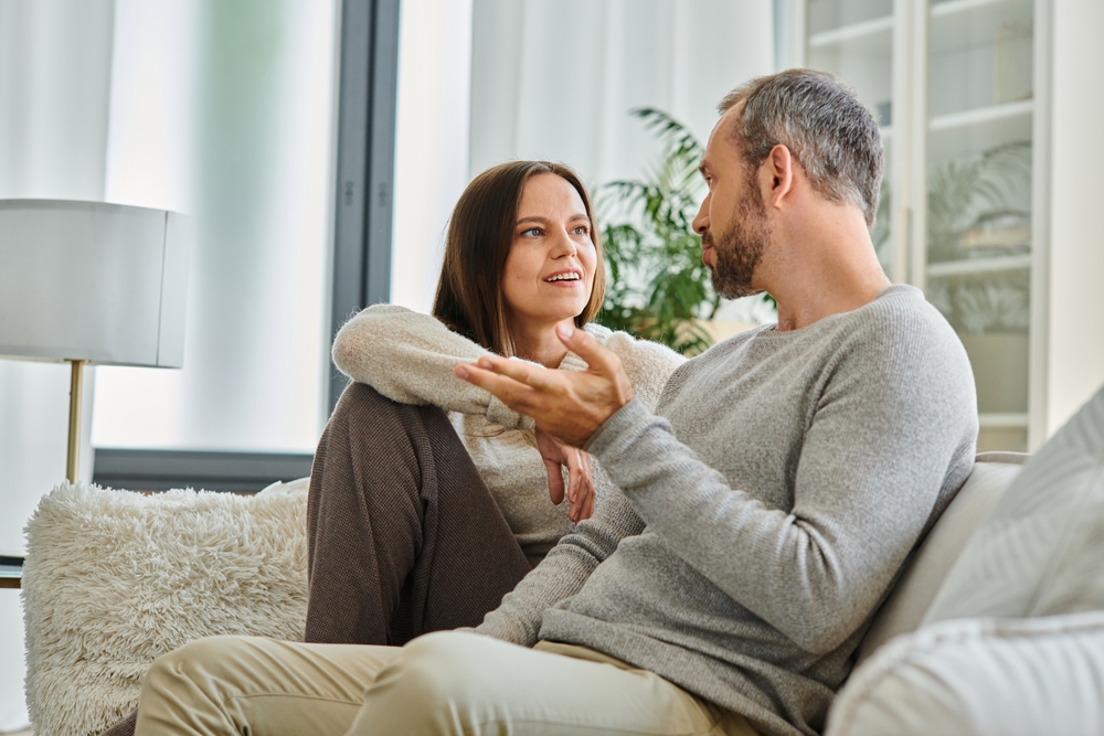 positive child-free couple talking on cozy couch in modern living room, quality time at home, banner