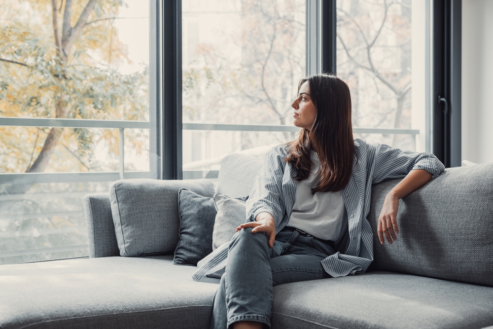 Portrait of happy dreamy young woman looking away, standing with folded arms in modern living room, visualizing future, recollecting good memories, planning weekend or thinking of problem solutions.
