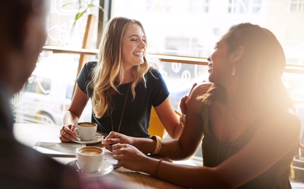 Laughing, friends or women in coffee shop for support, funny conversation or gossip news together. Happy, talking or people speaking of drinking espresso or tea in discussion or chat in cafe diner