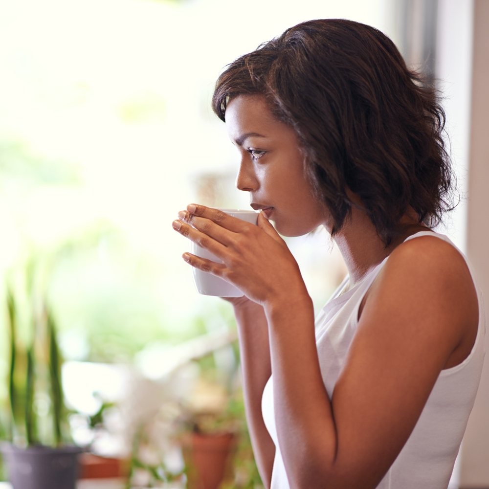 Woman, thinking and coffee in house for drink, morning and energy while planning schedule or agenda. Girl, idea and tea in home living room by window for peace of mind, breakfast and reflection
