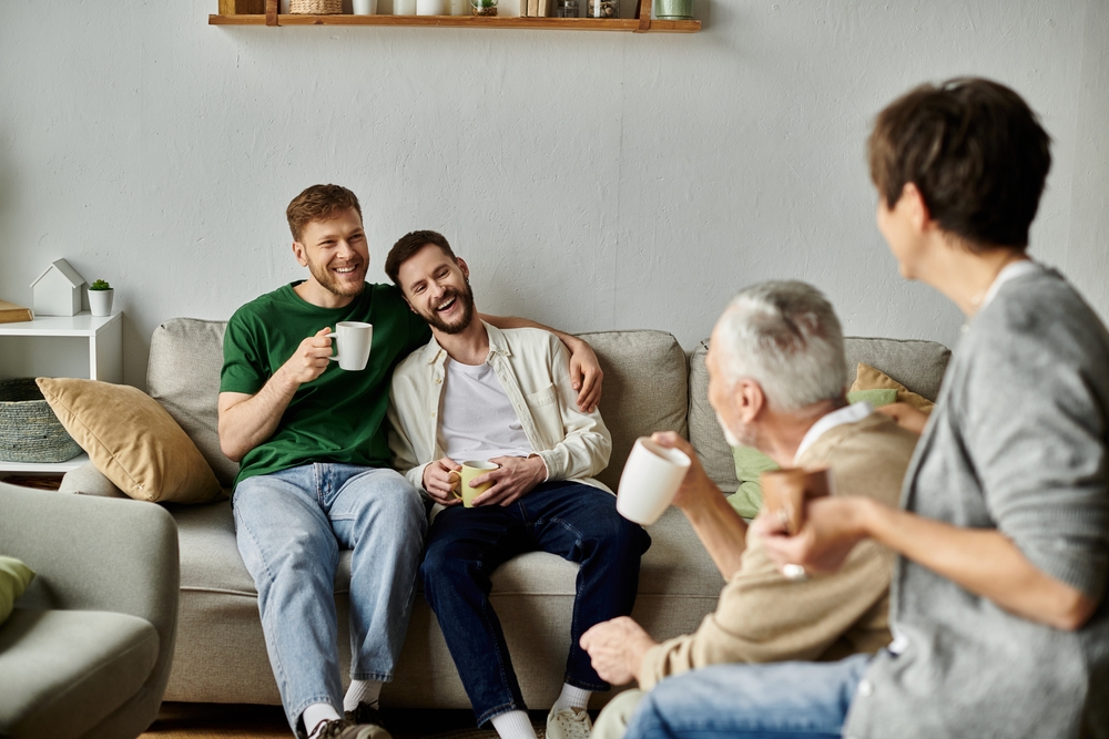 A gay couple enjoys coffee with parents in their living room.