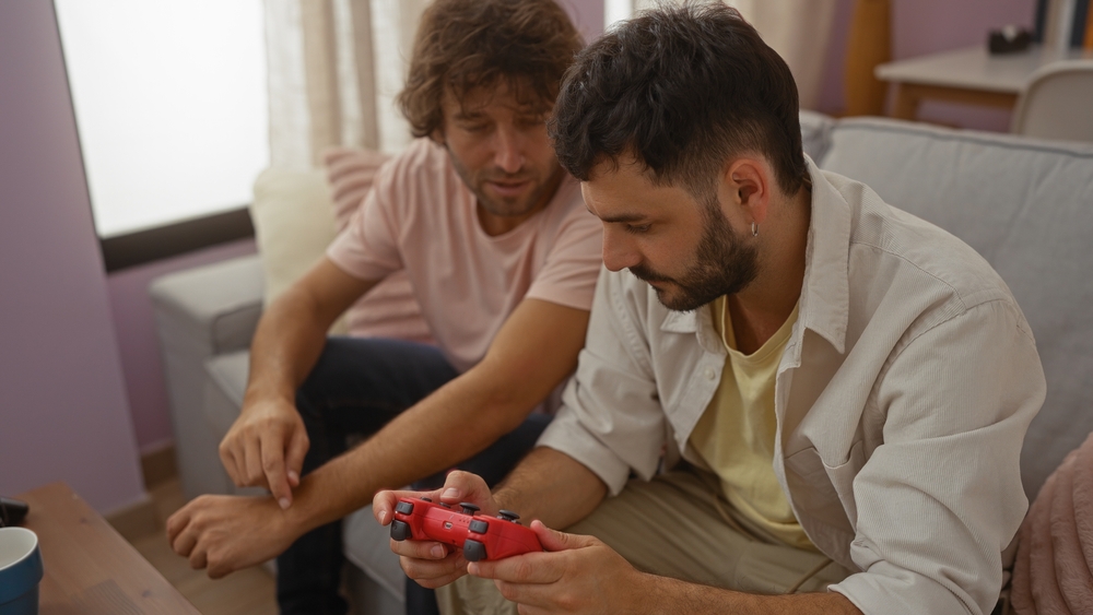 Two men sitting on a couch playing video games in a cozy living room, deep in conversation, suggesting a strong bond of friendship and family connection.