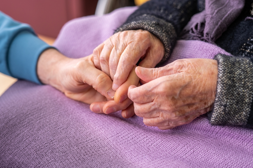 Caregiver Consoling Elderly Woman, Holding Hands With Empathy And Kindness, Senior Support And Compassionate Care In Nursing Home Environment