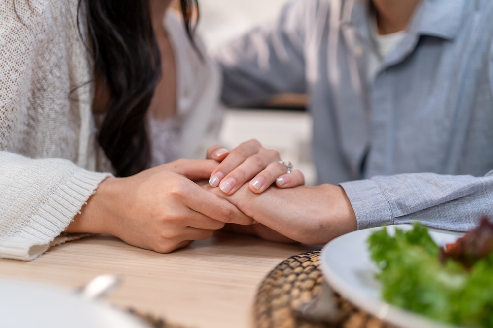 Close up of loving couple holding hands each other while eating foods in house. Attractive romantic new marriage man and woman celebrate anniversary and valentine's day on dining table at home.