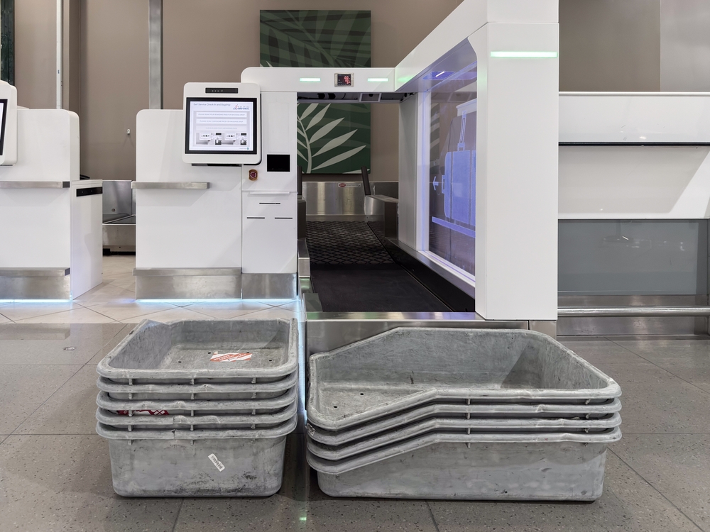 Penang, Malaysia - April 28, 2025: multiple gray metal bins stacked near a security check-in area. An automated luggage screening machine is visible in the background.