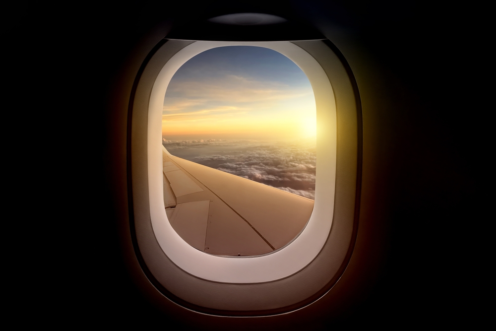 Airplane wing view from plane window over the landscape in sunlight. Summer background