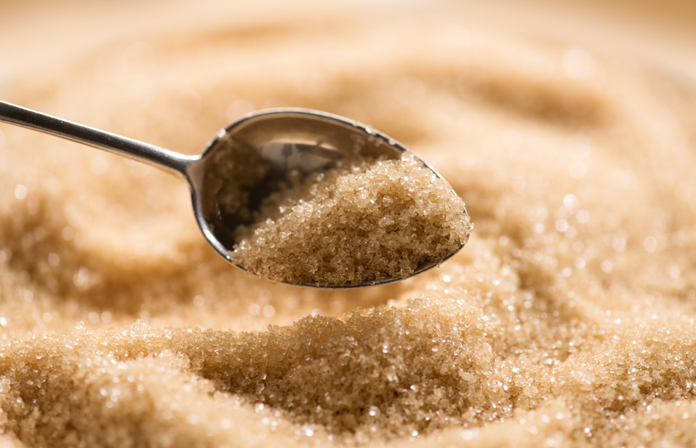 Brown Cane sugar in a spoon close up. Heathy eating, diet concept, macro shot. Granules of brown sugar in teaspoon closeup