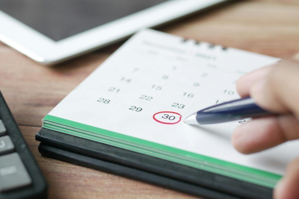 Desk calendar with the 30th circled in red ink, next to a tablet, pen, and calculator.