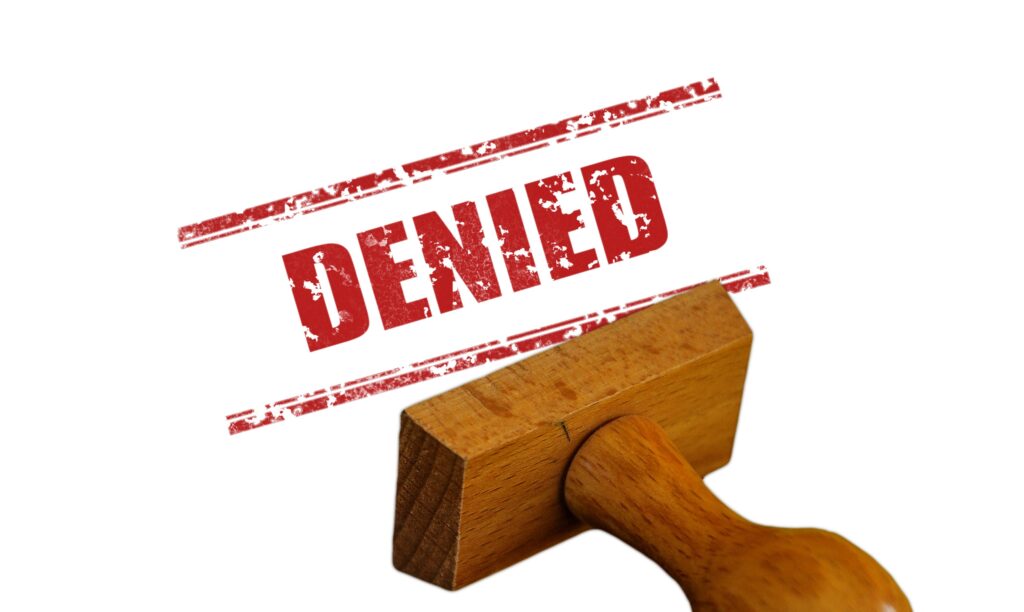 Bold red "DENIED" rubber stamp with a wooden handle pressed above its stamped imprint on a white background.