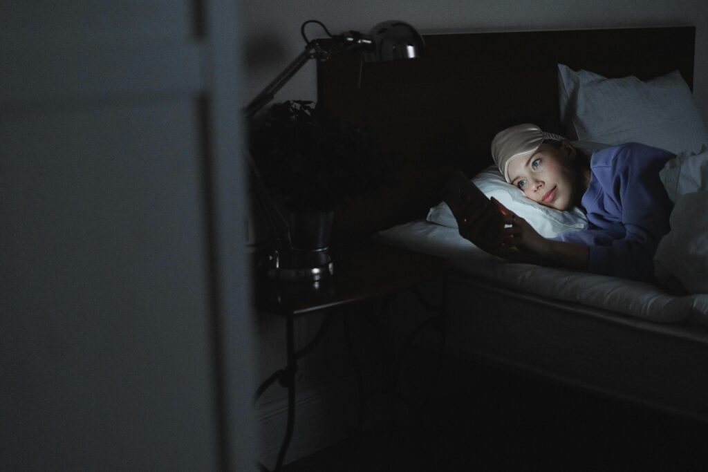 A young woman lying in bed at night, her face lit by the glow of the phone.