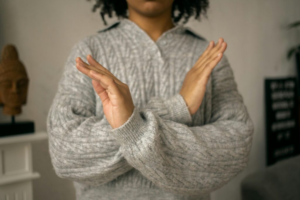 Close-up of a person in a grey knitted sweater crossing their arms in front of their chest, making a clear stop or no gesture.