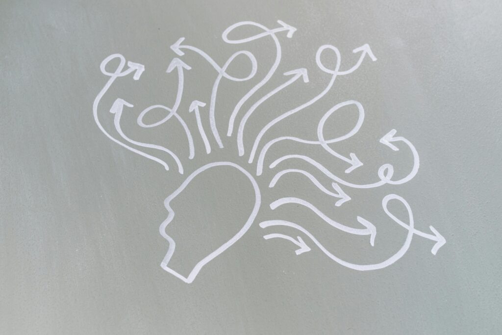 Chalk illustration of a human head in profile with multiple white arrows shooting outward in chaotic, looping directions.