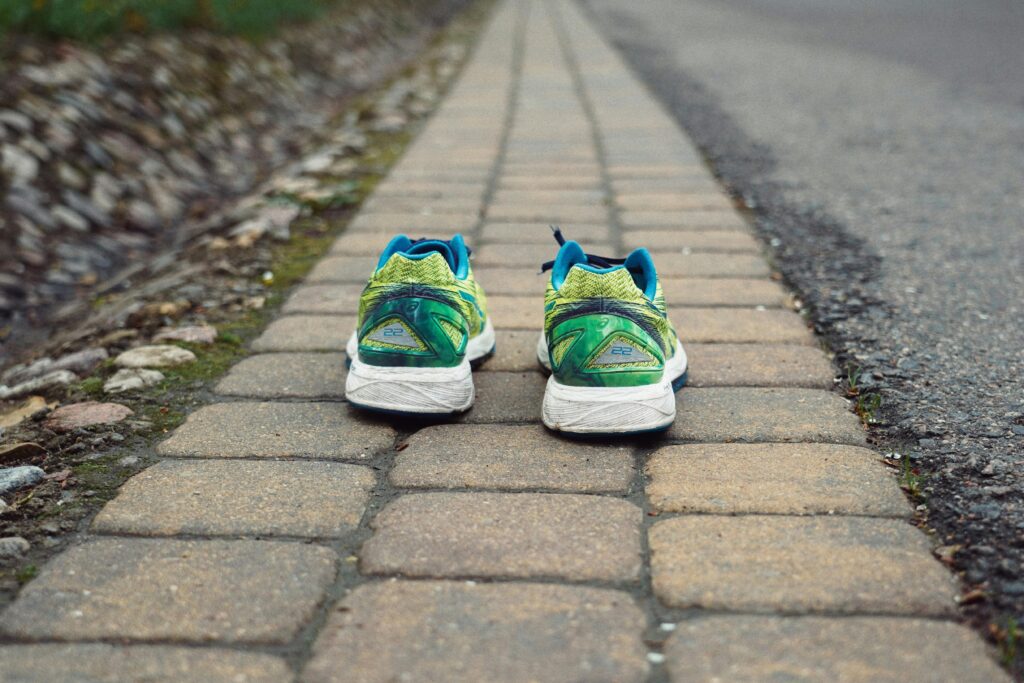 Pair of green and blue running shoes placed neatly on a brick pavement path.