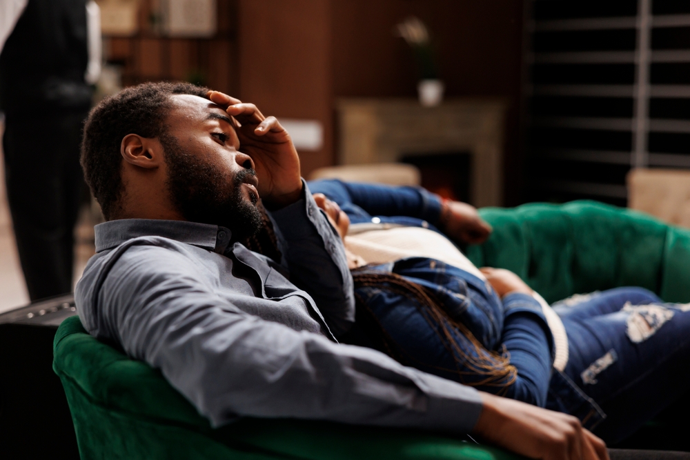 Tired sleepy man traveler feeling exhausted, suffering from headache after long air travel, unhappy tourist sitting in hotel lobby waiting for check-in. Jet lag disorder, travel fatigue