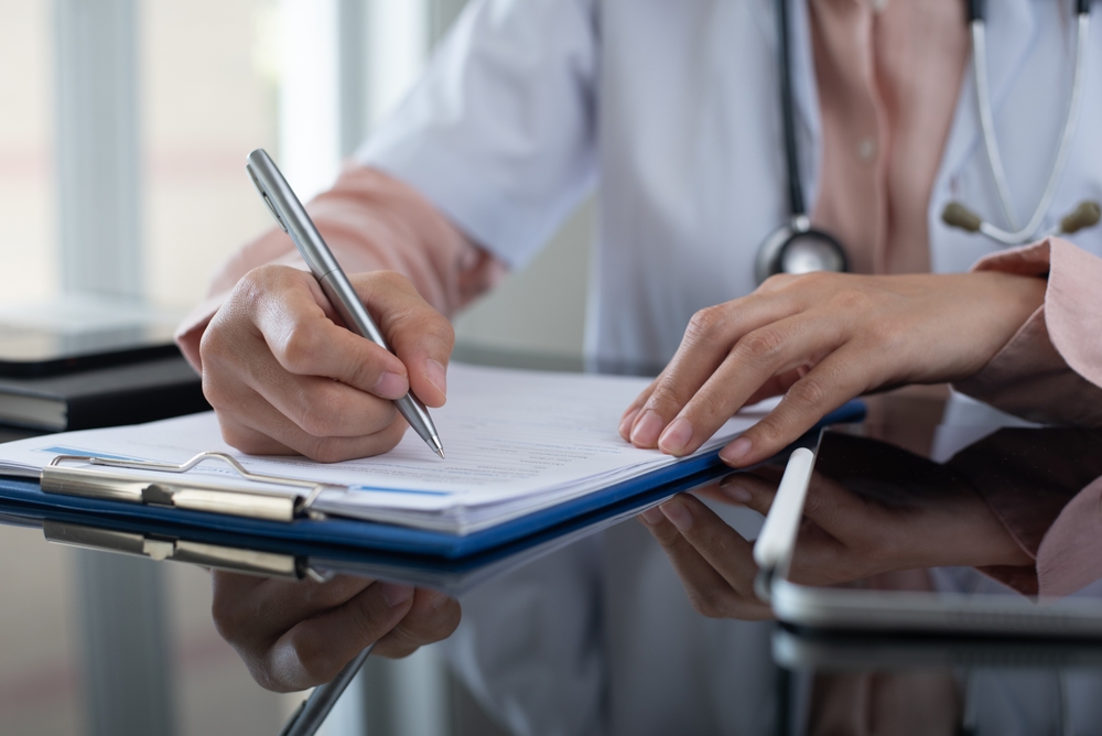 Asian woman doctor working and taking note information of patient on medical document on clipboard in medical room of hospital. Doctor filling insurance claim form or prescription