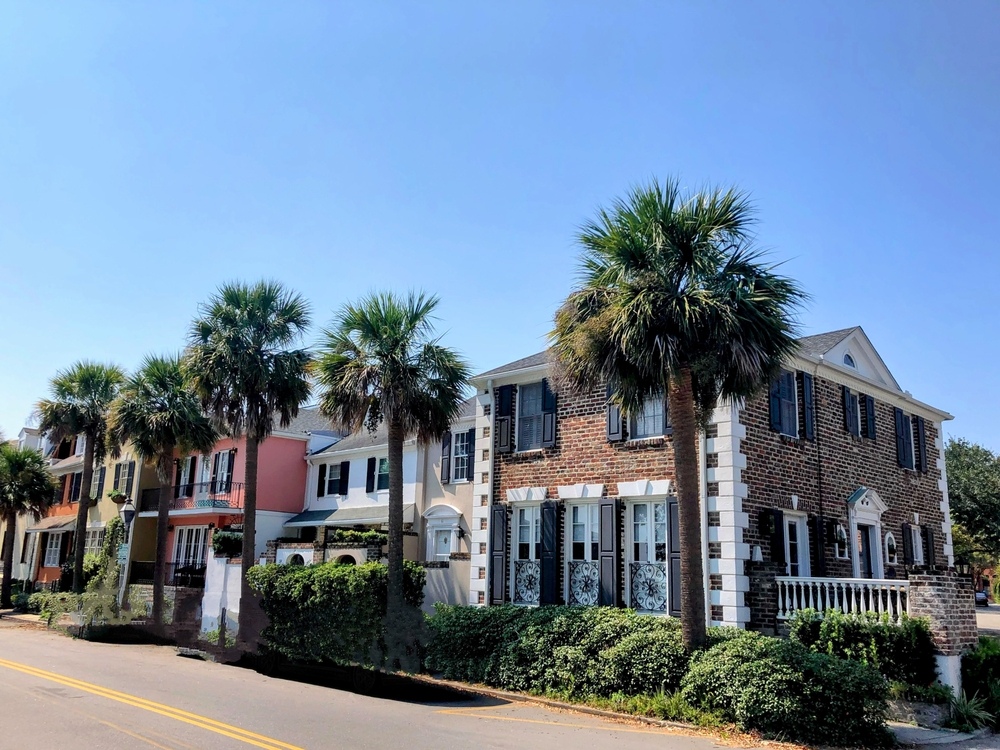 Charleston, South Carolina, USA – April 14, 2025: Brick and pastel townhouses with palm trees along a quiet residential street in Charleston’s historic district.