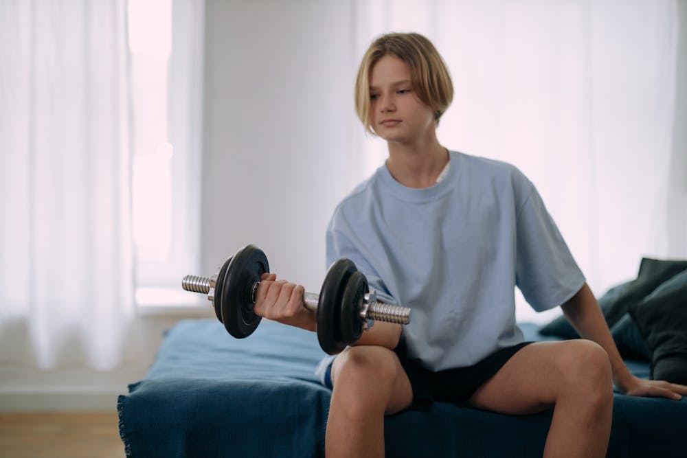 teen male lifting weights sitting on bed
