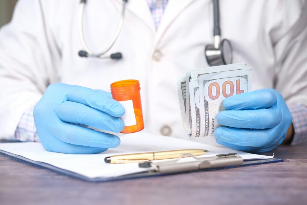 Medical professional wearing blue gloves and a white coat, holding an orange prescription pill bottle in one hand and a stack of hundred-dollar bills in the other.