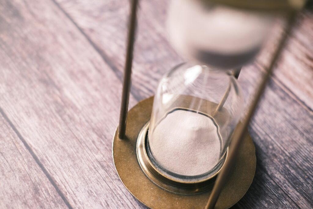 Hourglass with sand flowing through its narrow center, placed on a weathered wooden surface.