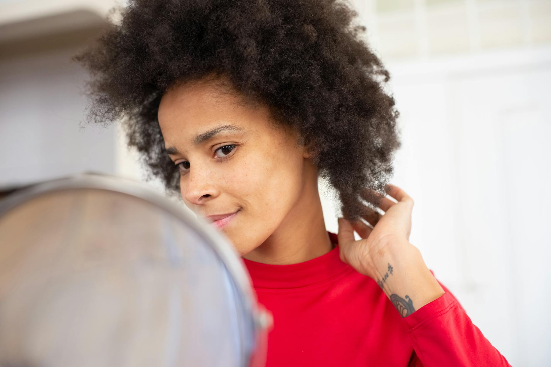 Confident woman with afro hairstyle glancing in the mirror, adjusting her hair indoors.