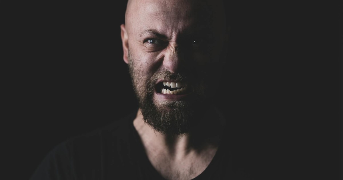 Close-up of a bald and bearded man showing a fierce expression in a dark setting.