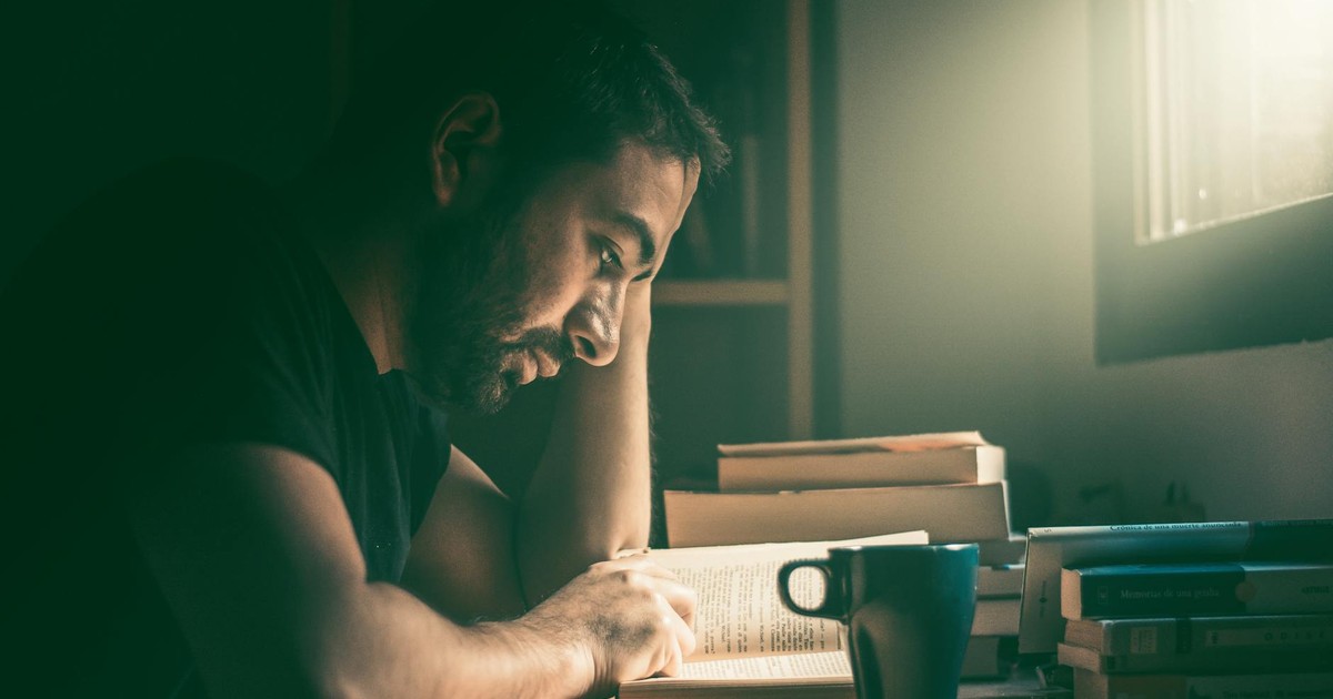 An adult man immersed in reading by the window in Madrid. Warm, focused study atmosphere.