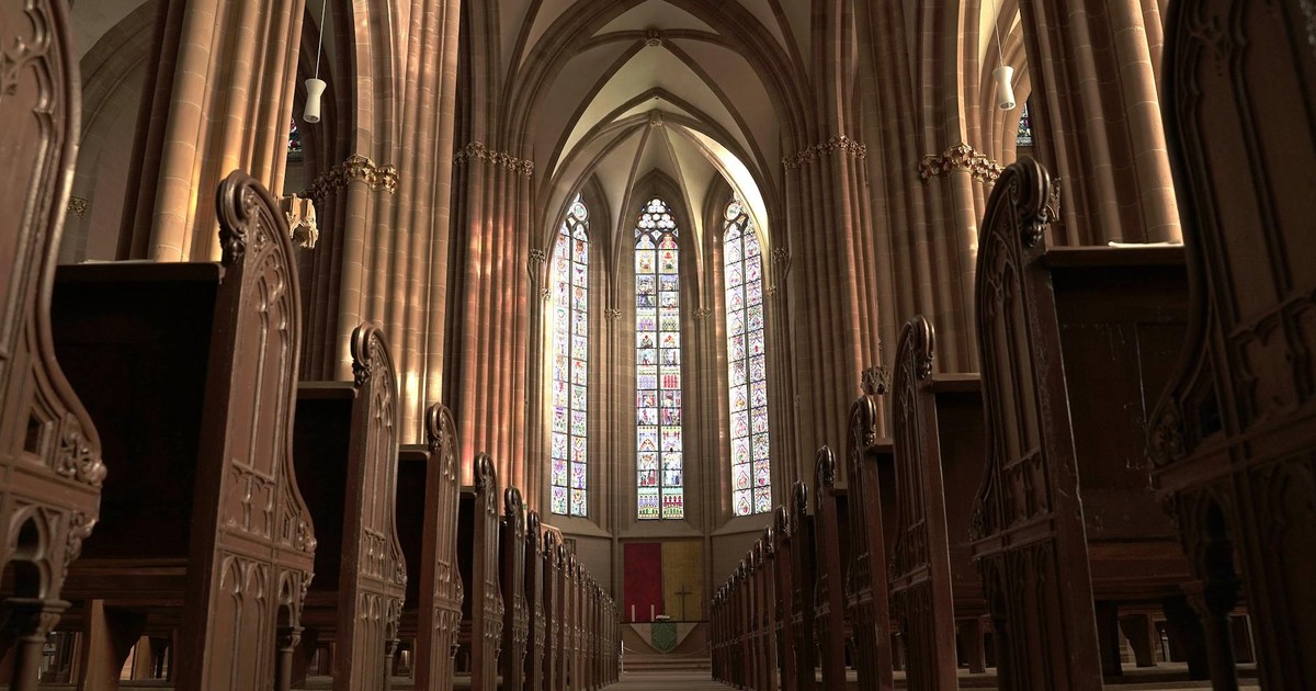 Interior view of a gothic church in Oppenheim, showcasing arches, pews, and stained glass windows.