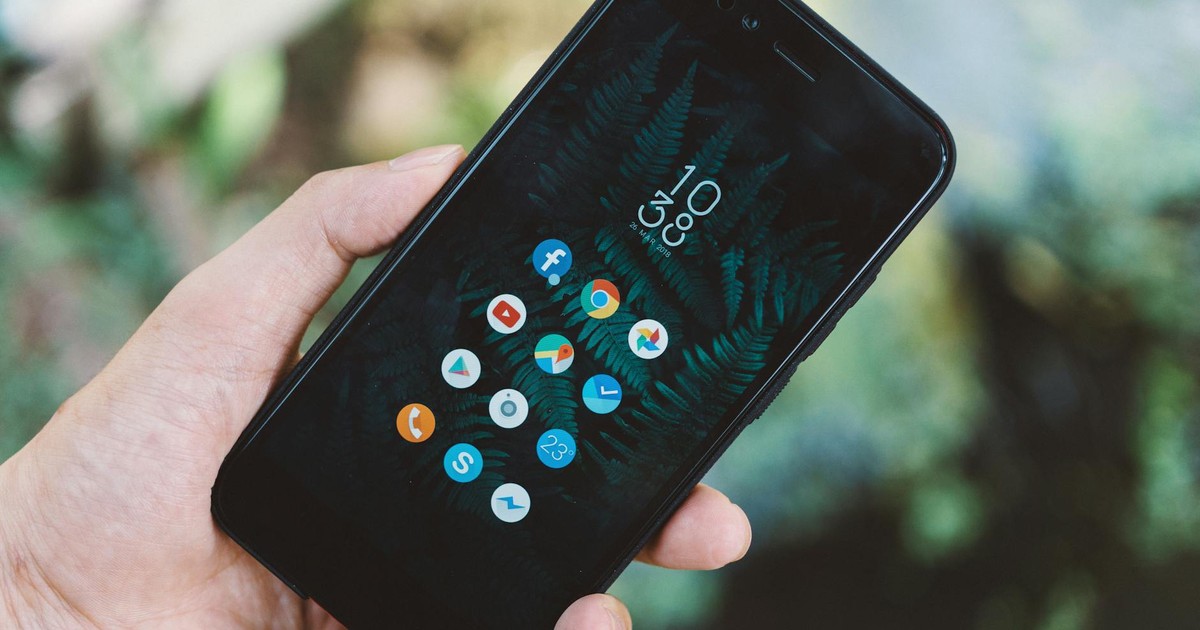 Close-up of a hand holding a smartphone with app icons and a nature wallpaper.