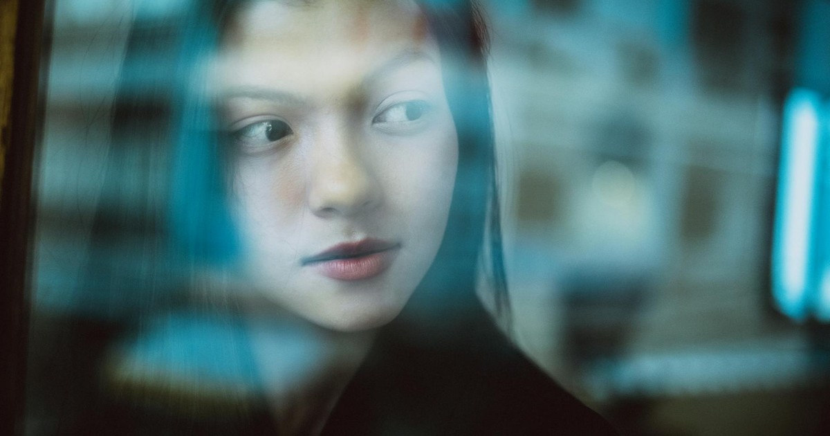 Through glass wall view of crop young ethnic female with makeup looking away in daytime