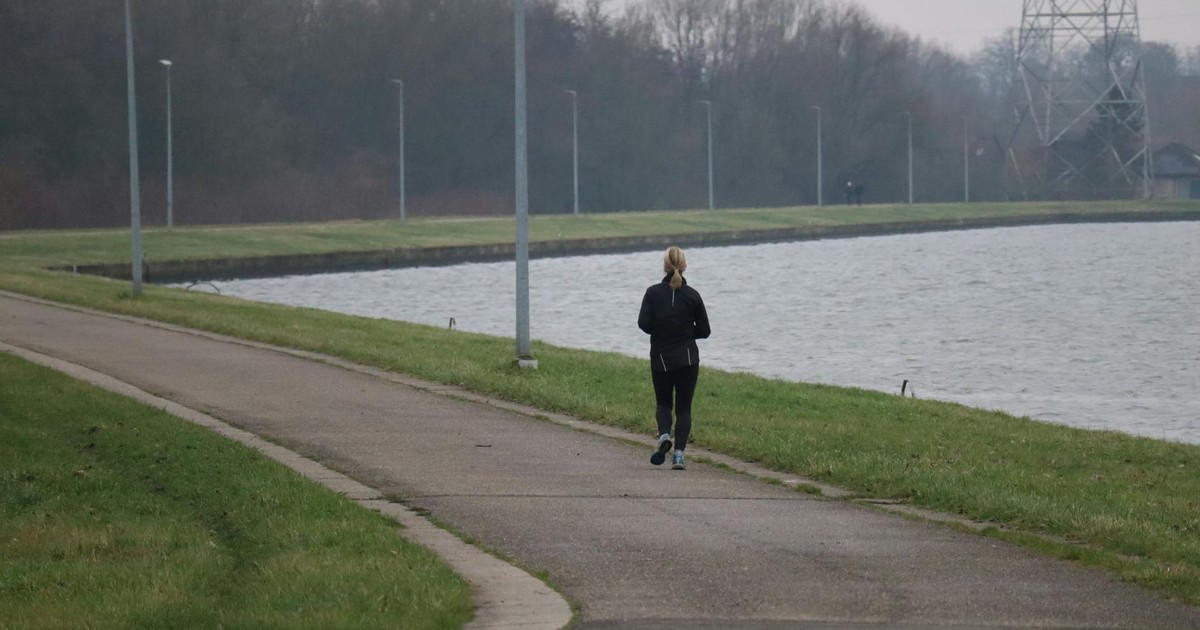 A woman jogs on a scenic pathway beside the water, embodying fitness and wellness.