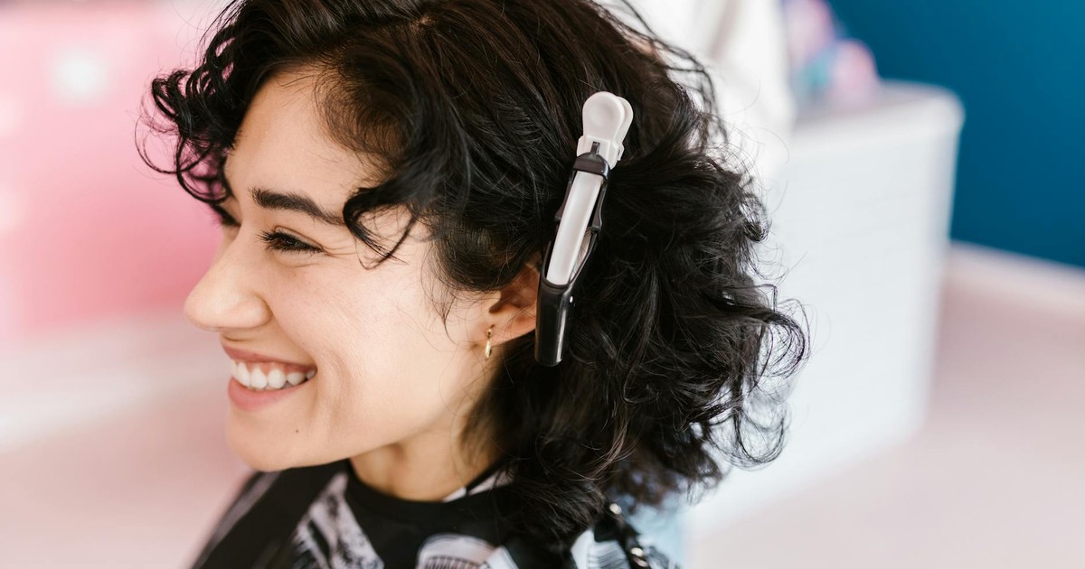 Side profile of a woman with curly hair smiling in a hair salon with a hair clip.