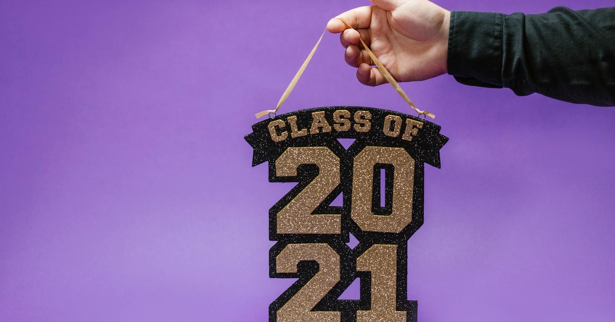 Glittery 'Class of 2021' sign held by a hand against a purple background.