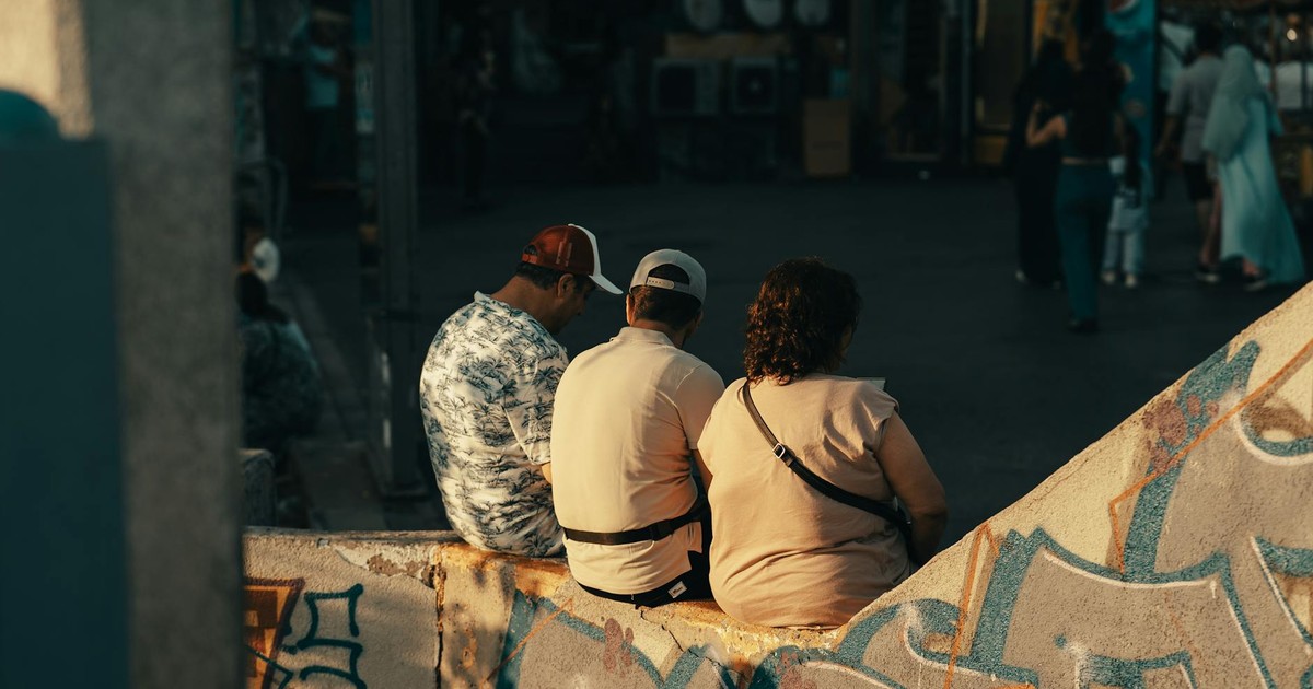 Three people sit on a graffiti-covered wall in an urban setting, capturing a moment of leisure.