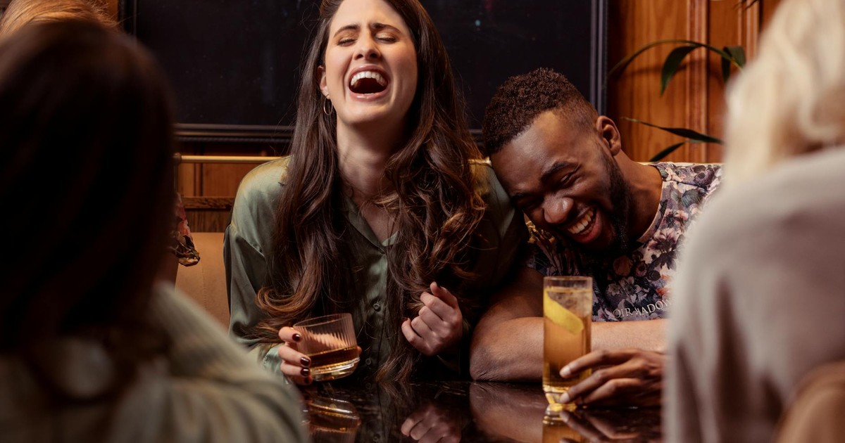 Lively friends laughing and enjoying drinks together at a cozy indoor setting.