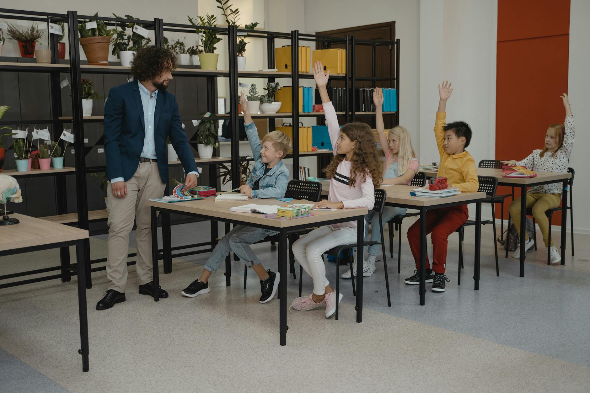Children actively participating by raising hands during a class session, guided by their teacher.