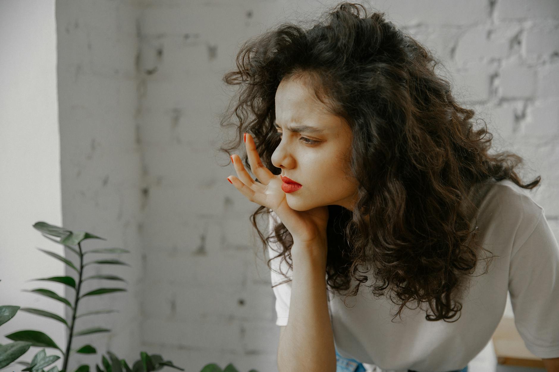 A thoughtful young woman with curly hair indoors, displaying a curious expression.