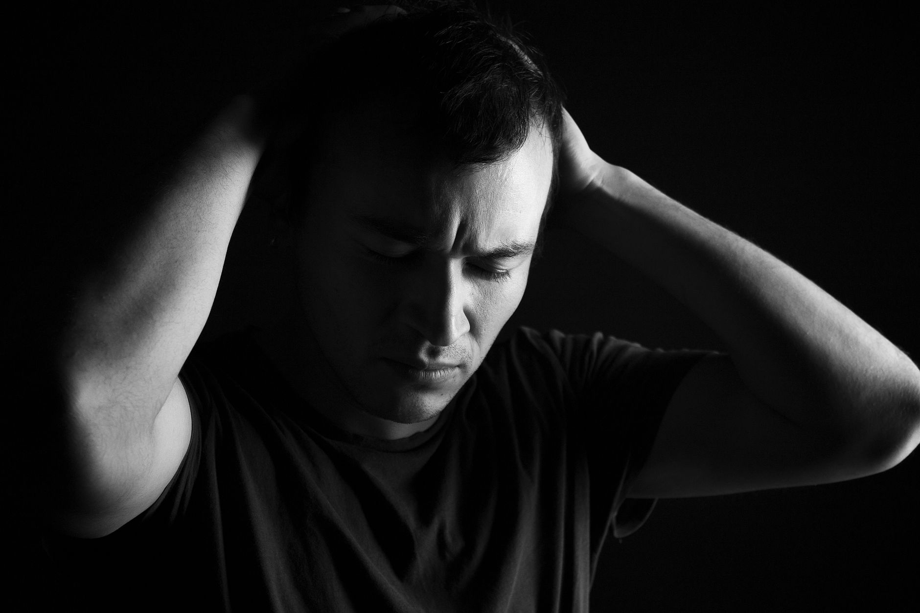 A black and white portrait capturing a distressed man with hands on head, conveying anxiety.