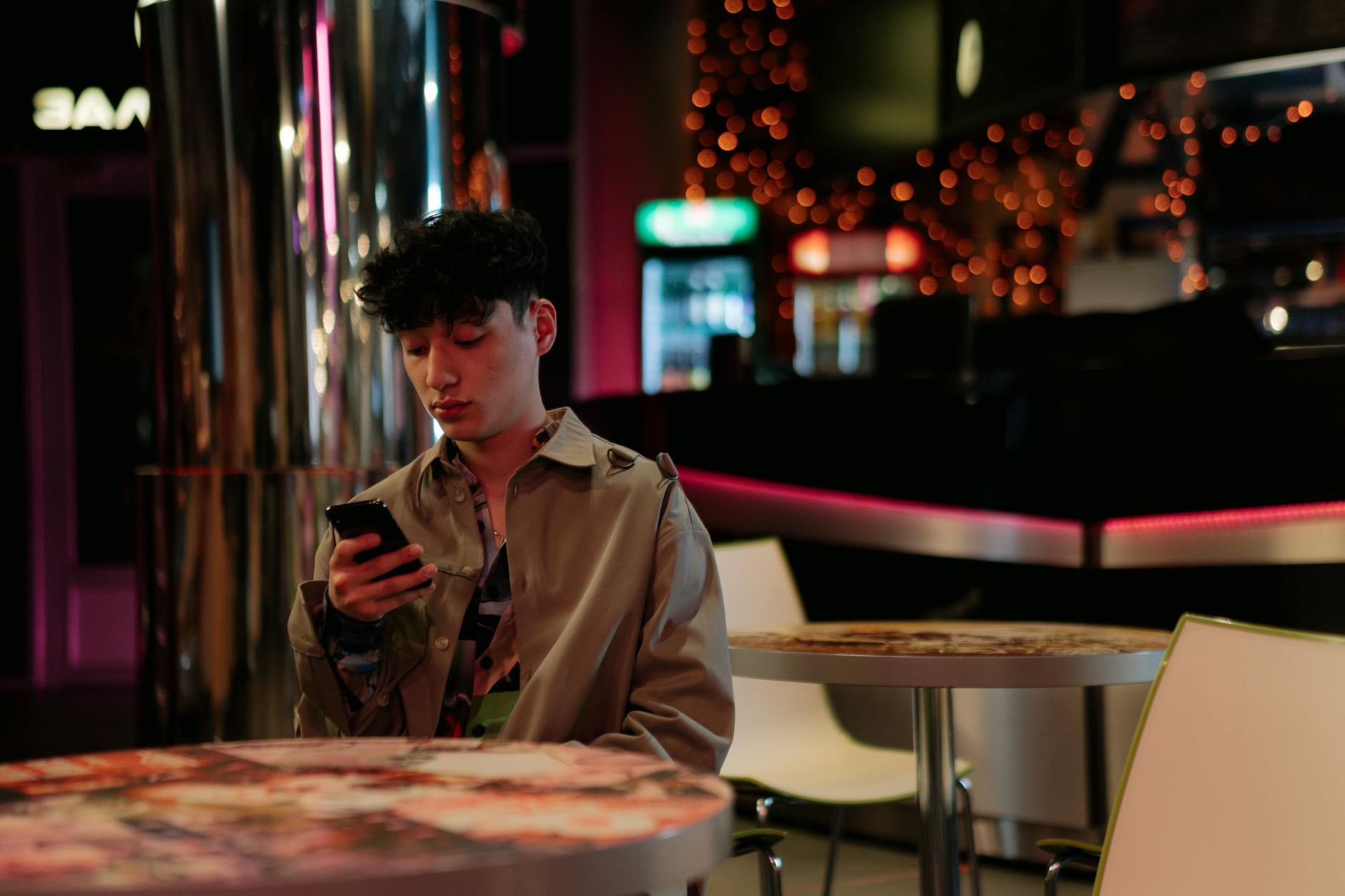 A young man focused on his smartphone in a chic indoor setting with ambient lighting.