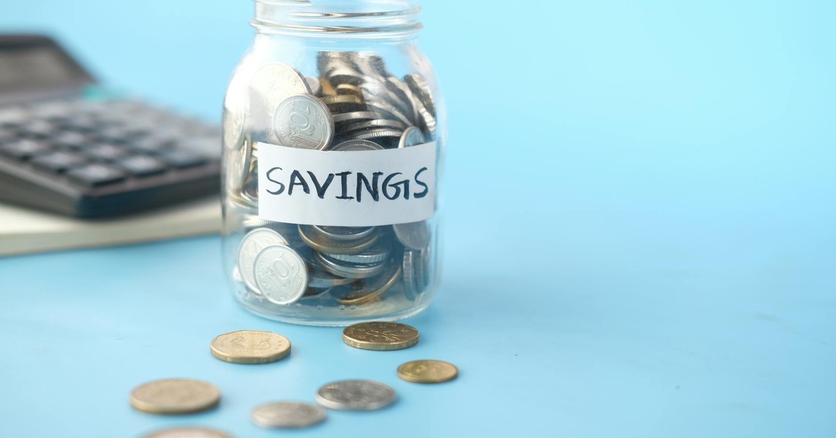 Glass jar labeled 'Savings' filled with coins, beside a calculator on a blue background.