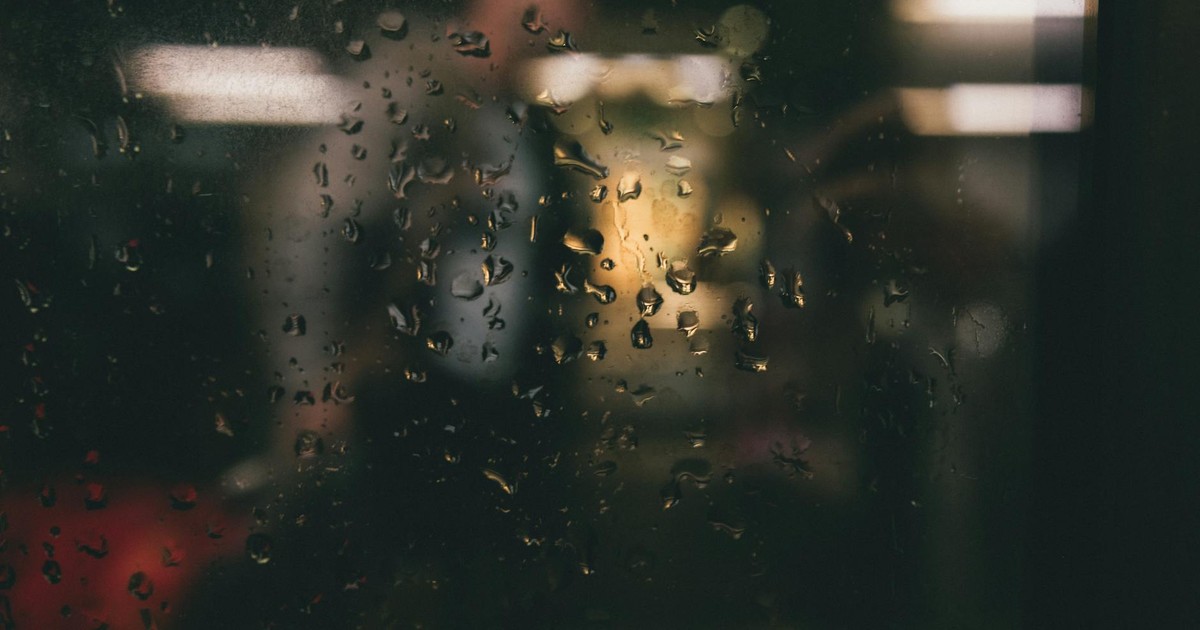Raindrops on a window create a moody, blurred view of an indoor scene.