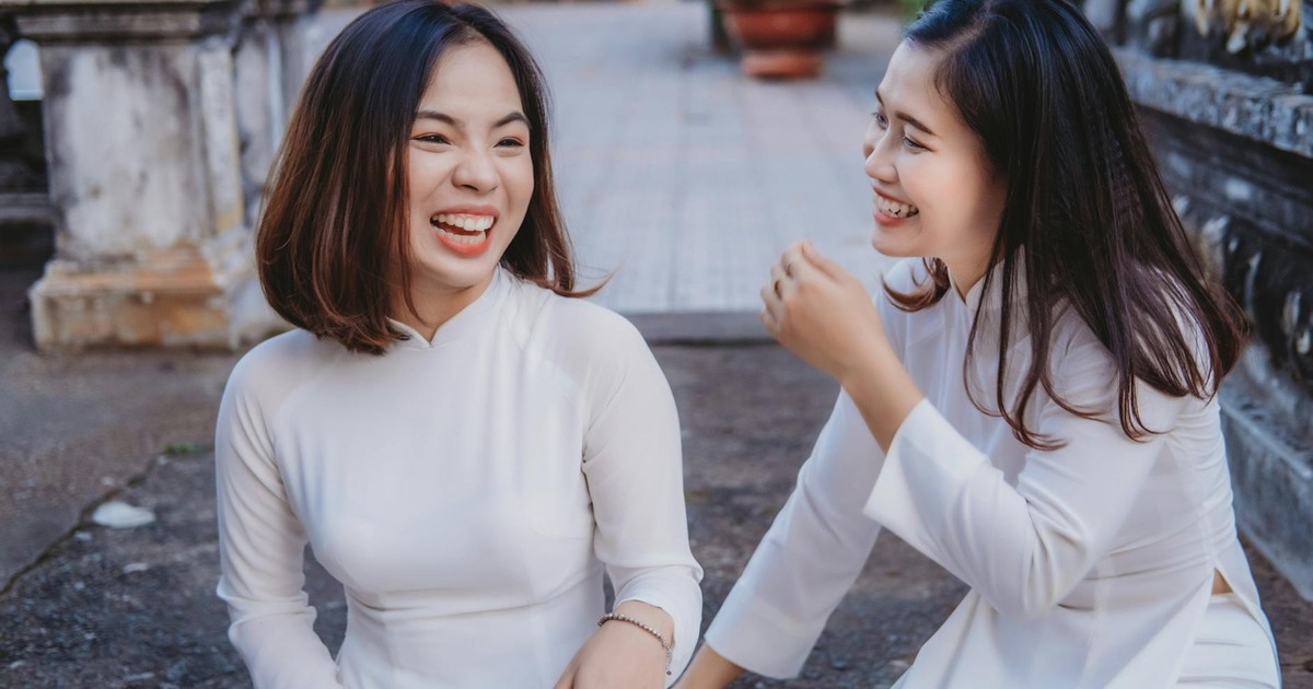 Two Vietnamese women in traditional attire laughing and enjoying a joyful moment outdoors.