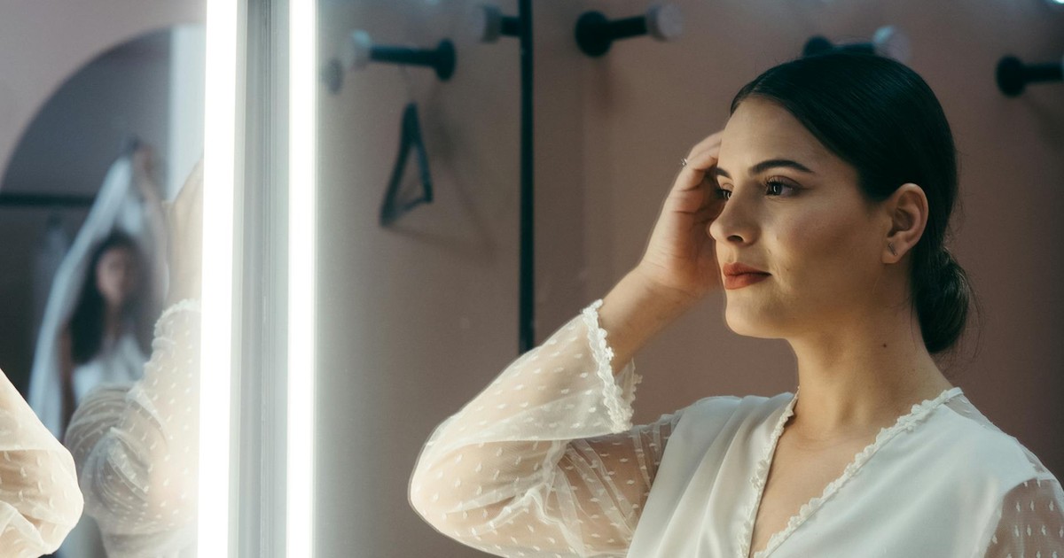 A bride admires herself in the mirror, prepping for her wedding day with elegance and poise.