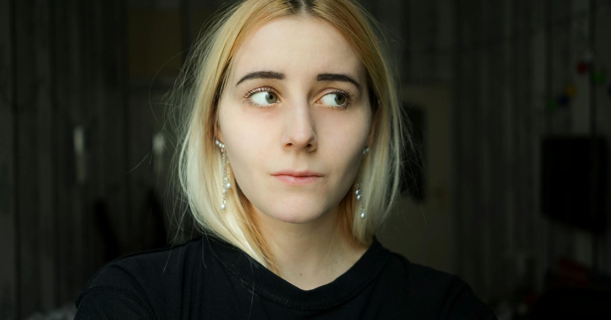 Pensive calm female in black casual outfit standing in dark room and looking away dreamily