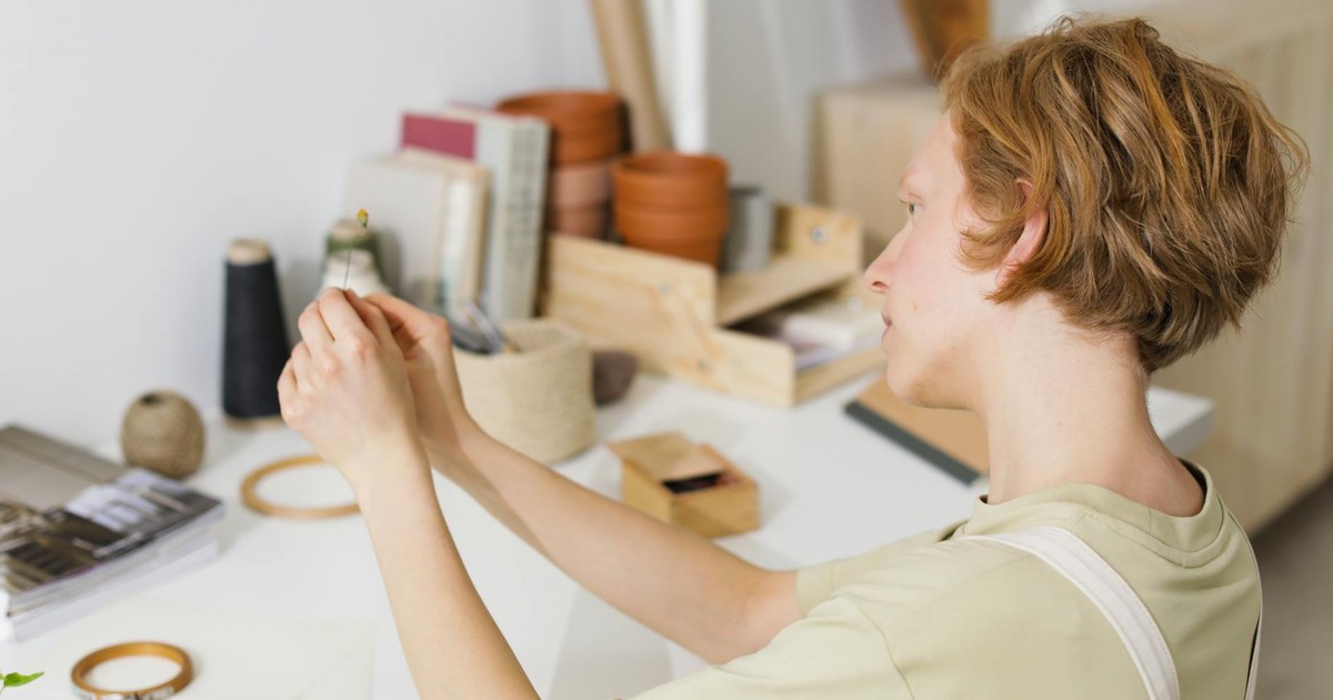 Caucasian woman crafting in a minimalist workspace with sewing supplies and plants.