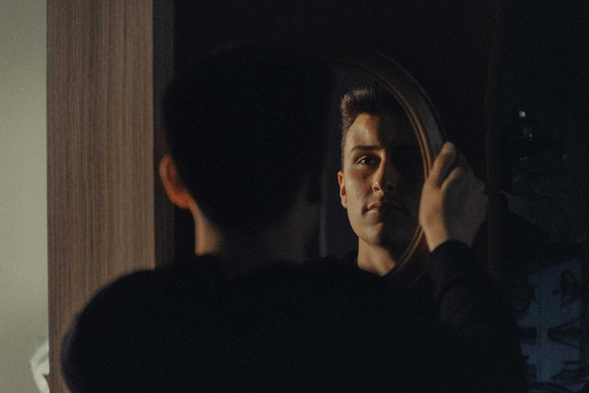 A man gazing at his reflection, capturing an introspective moment indoors.