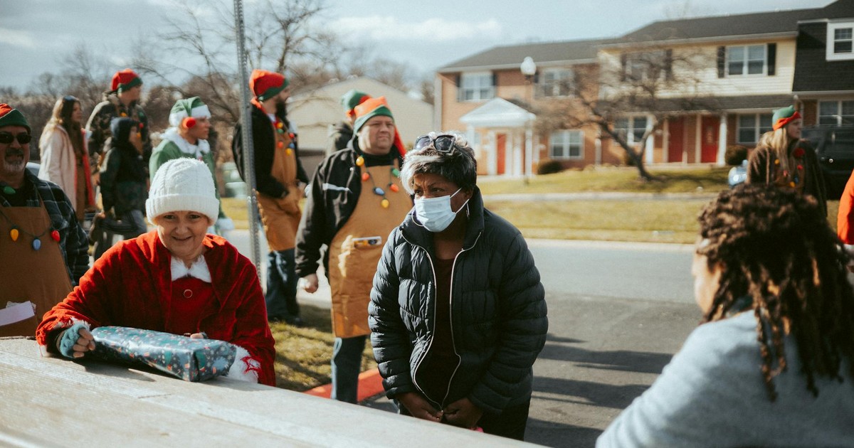 A neighborhood holiday gathering featuring adults dressed in elf costumes distributing gifts on a street.